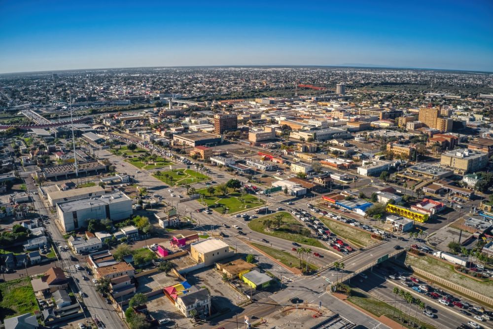 Aerial view of a cityscape with buildings, roads, and greenery under a clear blue sky.