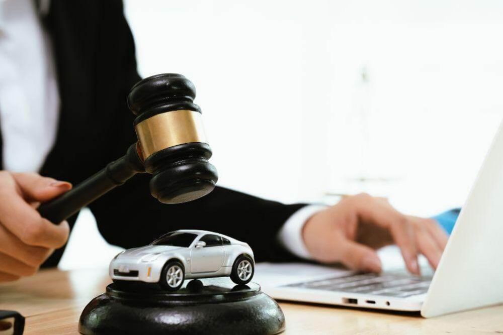 a person sitting at a desk with a laptop and a toy car on top of