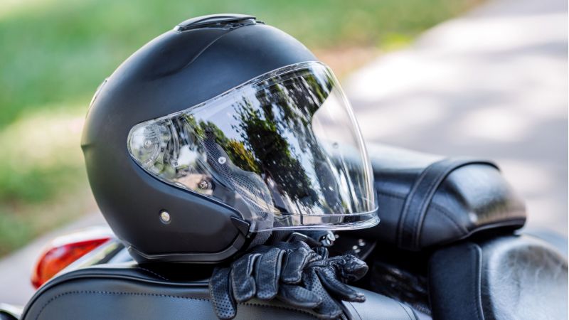 Black motorcycle helmet and protective gloves resting on a motorcycle seat.
