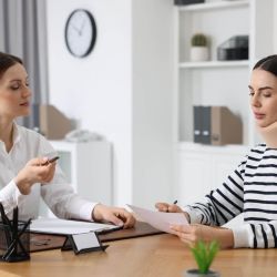 Clinician explains documents to a patient wearing a neck brace in a bright office.