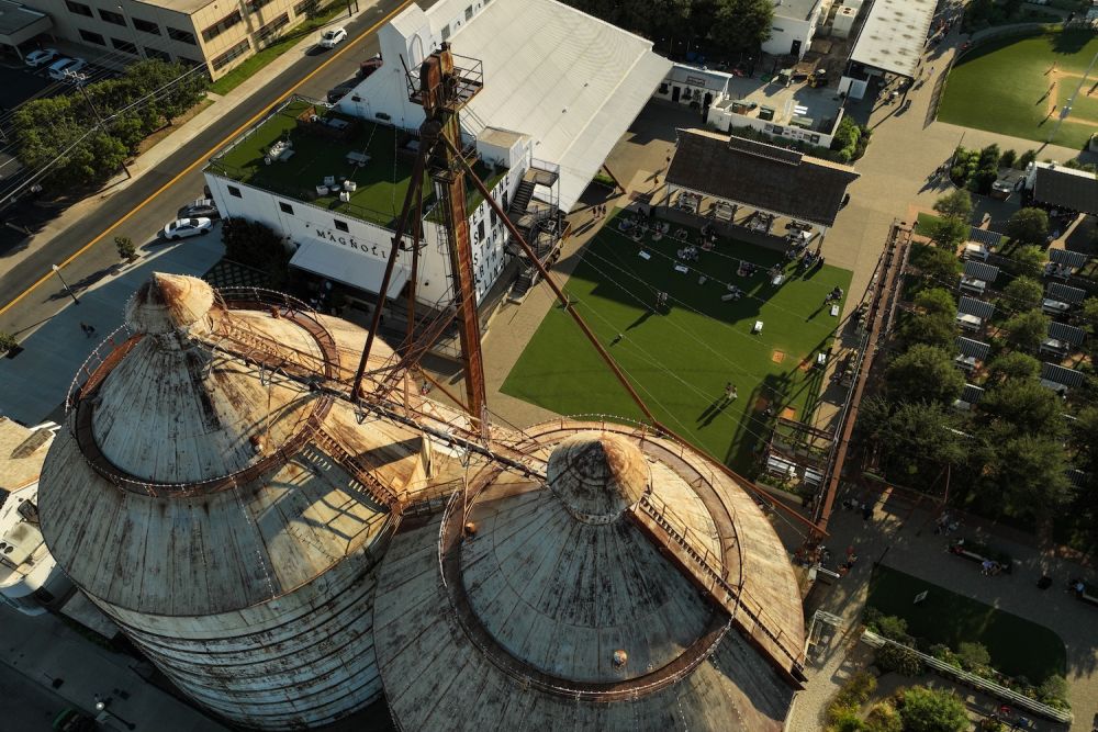 Aerial view of historic silos at Magnolia Market in Waco, Texas, showcasing surrounding green spaces and buildings.