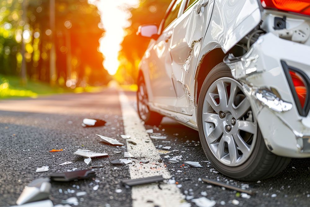 Damaged car on a road with debris, highlighting crash aftermath and accident scene in the sunlight.