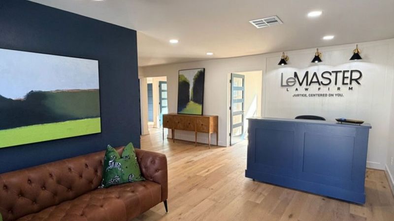 Modern law firm lobby with a blue reception desk, leather sofa, and abstract art on walls.