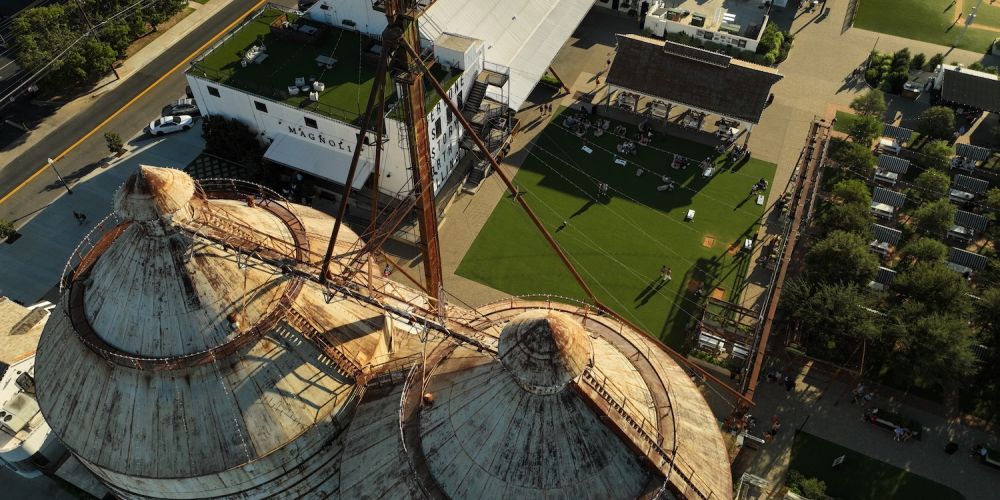 Aerial view of historic silos at Magnolia Market in Waco, Texas, showcasing surrounding green spaces and buildings.