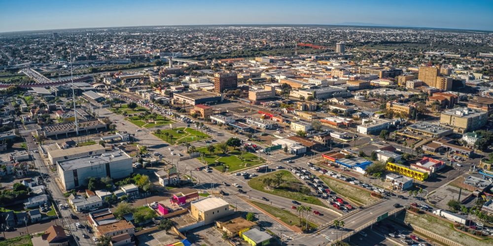 Aerial view of a cityscape with buildings, roads, and greenery under a clear blue sky.