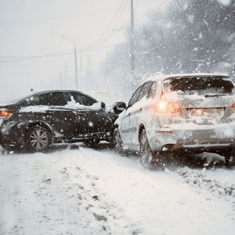 Two cars collide on a snow-covered road during heavy snowfall, highlighting winter driving hazards.