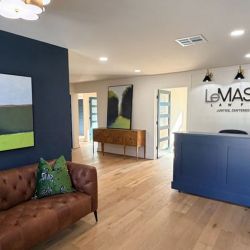 Modern law firm lobby with a blue reception desk, leather sofa, and abstract art on walls.