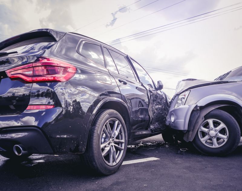 Two SUVs in a head-on collision on a cloudy day, showing severe vehicle damage on both fronts.