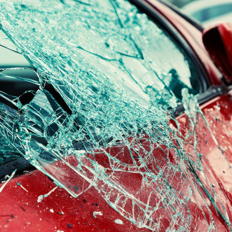 Shattered car window on a red vehicle, close-up view showing damage and broken glass details.