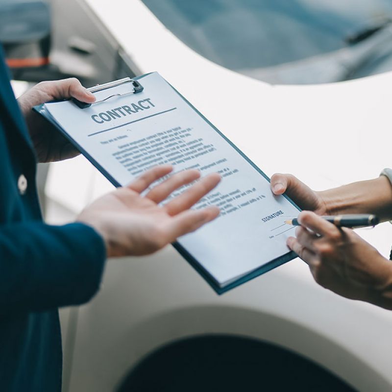 Person signing a contract on a clipboard outside, suggesting business agreement or deal completion.