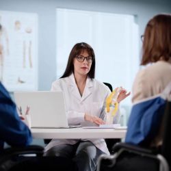 a woman in a white lab coat sitting at a table with a laptop
