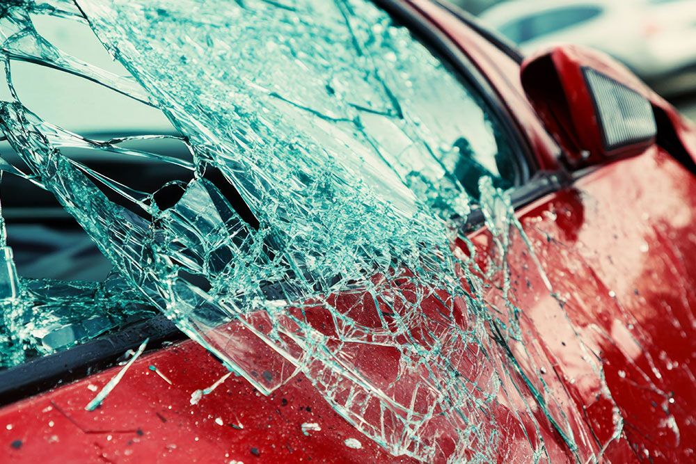 Shattered car window on a red vehicle, close-up view showing damage and broken glass details.