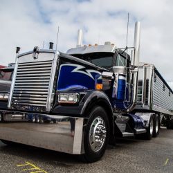Shiny blue and chrome semi-truck parked at a truck show under a cloudy sky.
