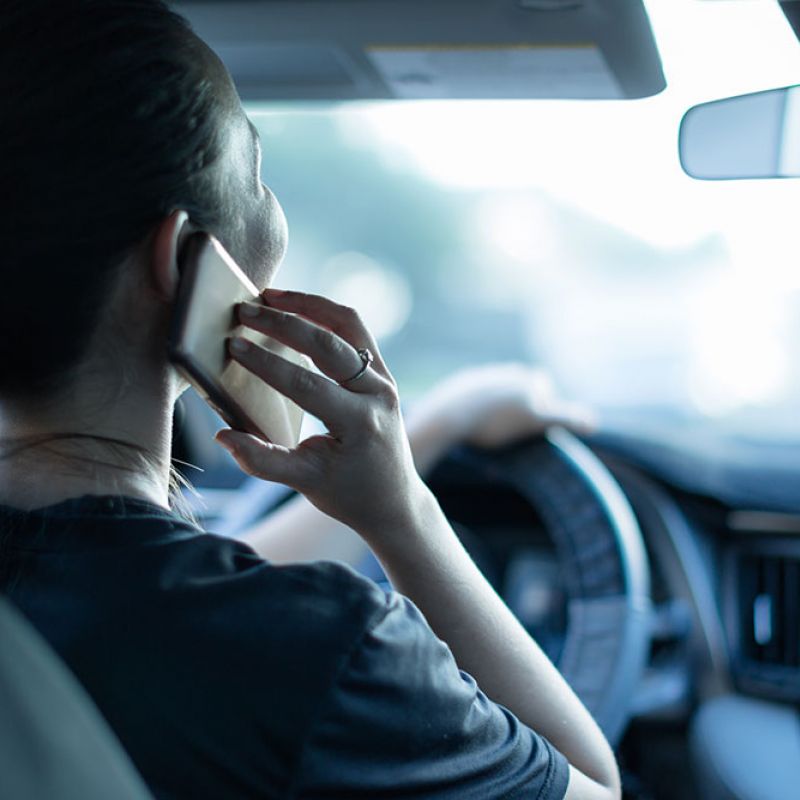 Person driving a car while talking on a smartphone, showcasing distracted driving for safety awareness.