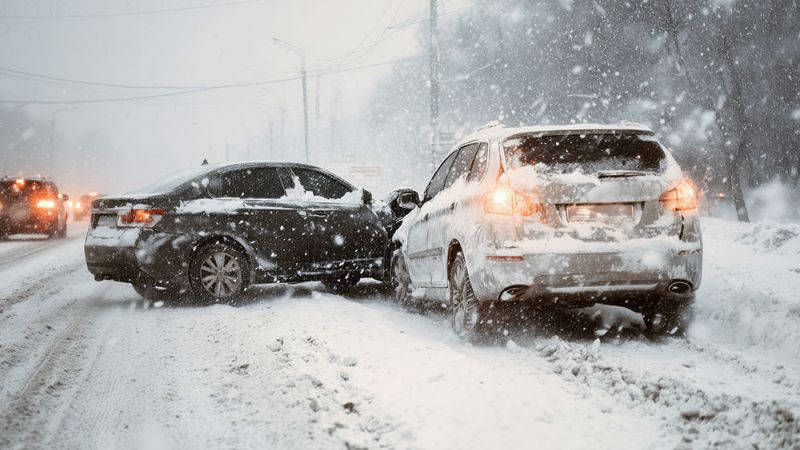 Two cars collide on a snow-covered road during heavy snowfall, highlighting winter driving hazards.