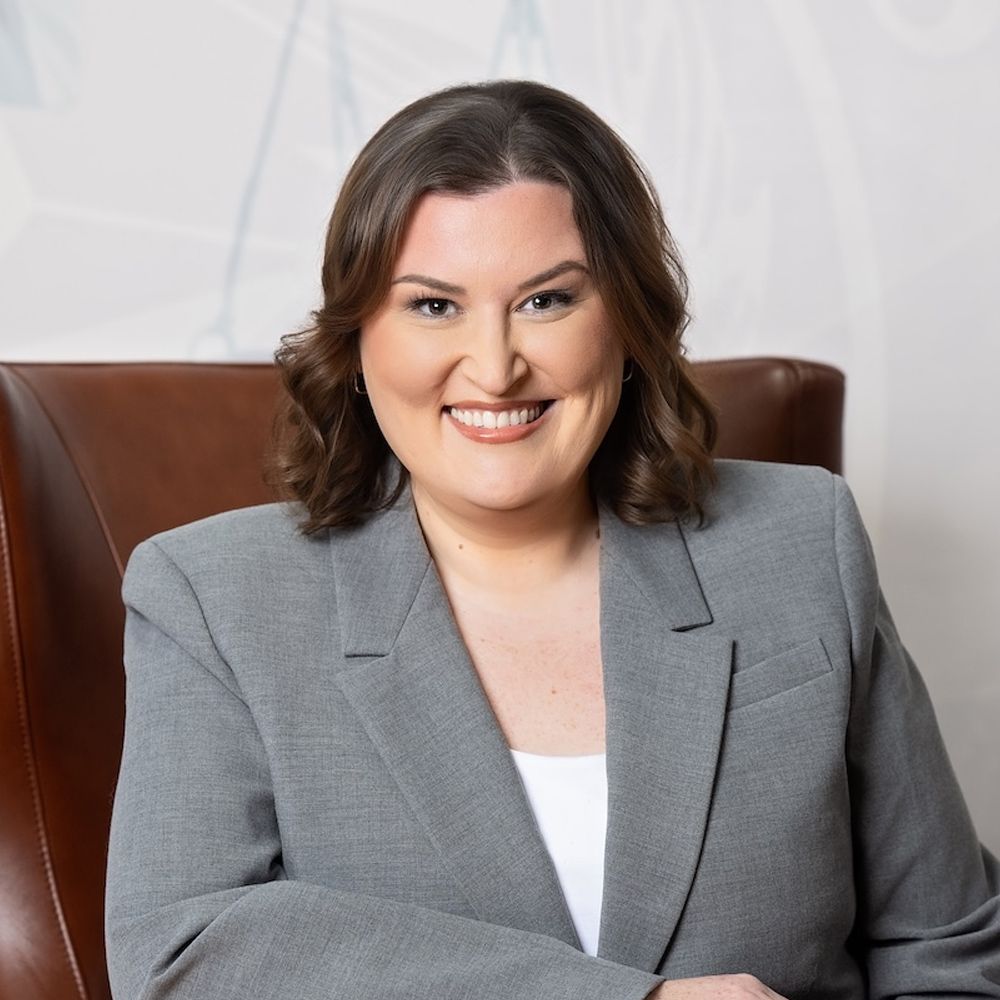 Abbie G. Berger in a gray blazer sitting on a leather chair, suitable for professional headshot or business profile.