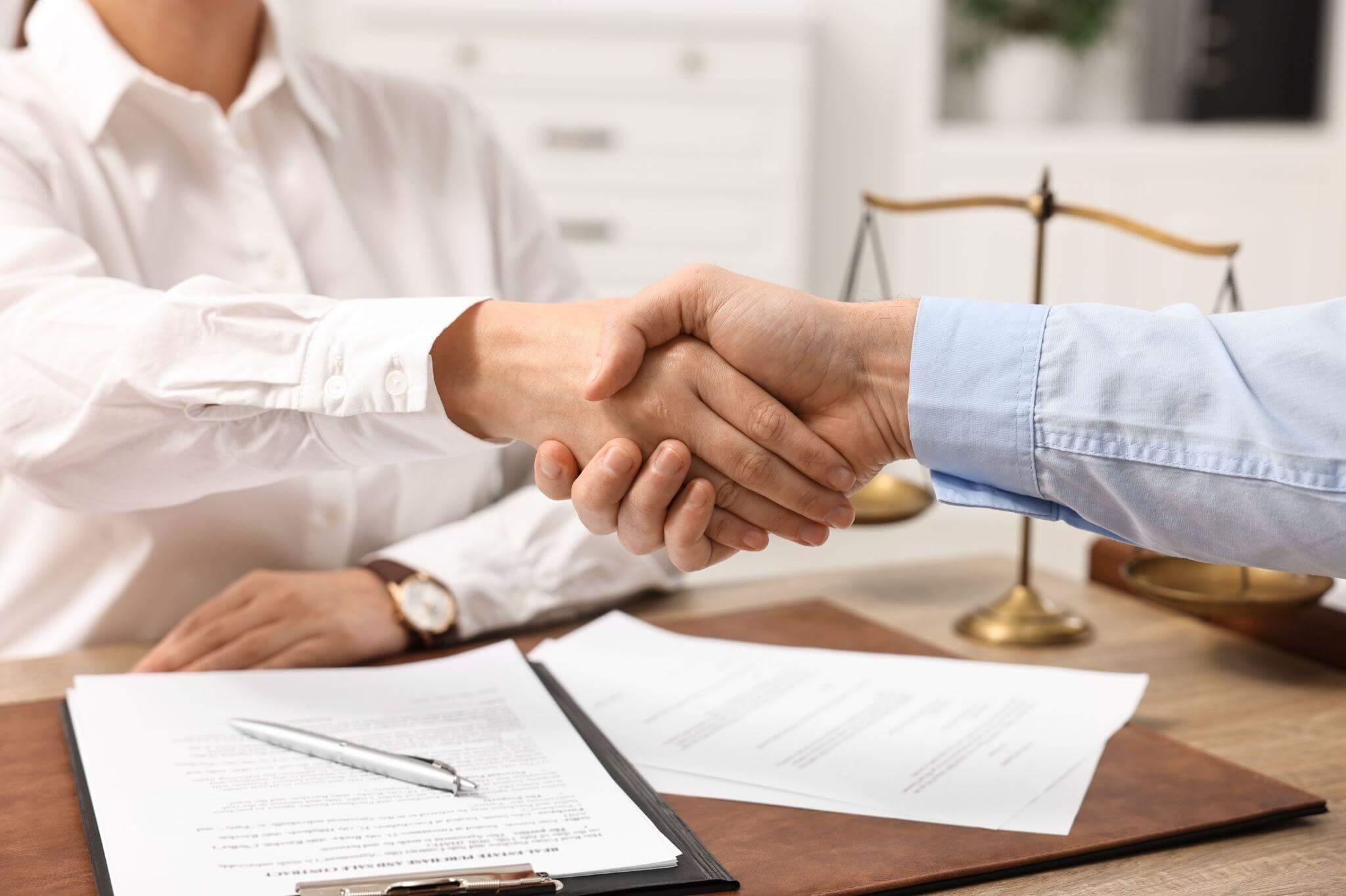 two people shaking hands over papers on a desk