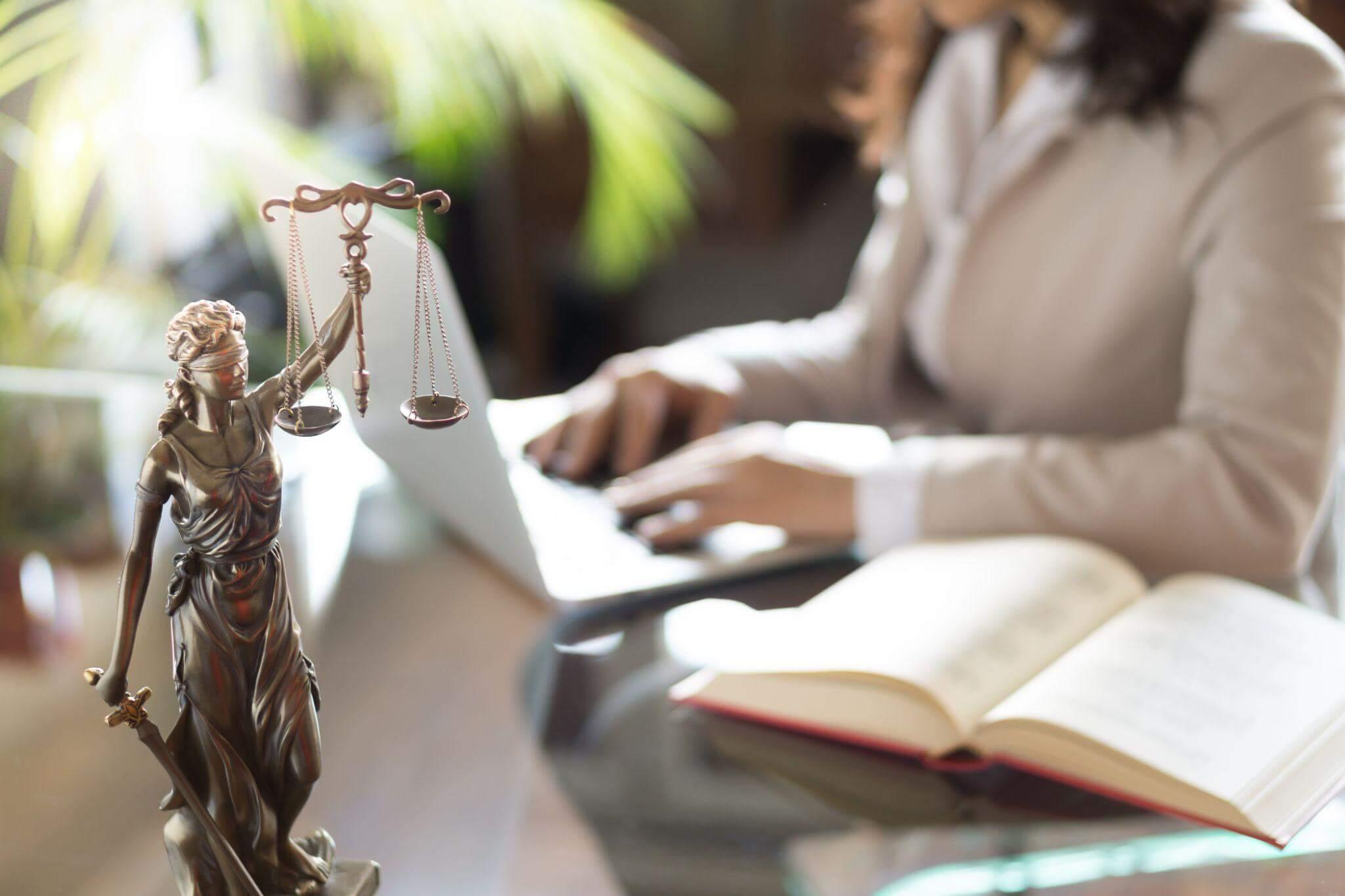 Woman at table with book and Lady Justice statue