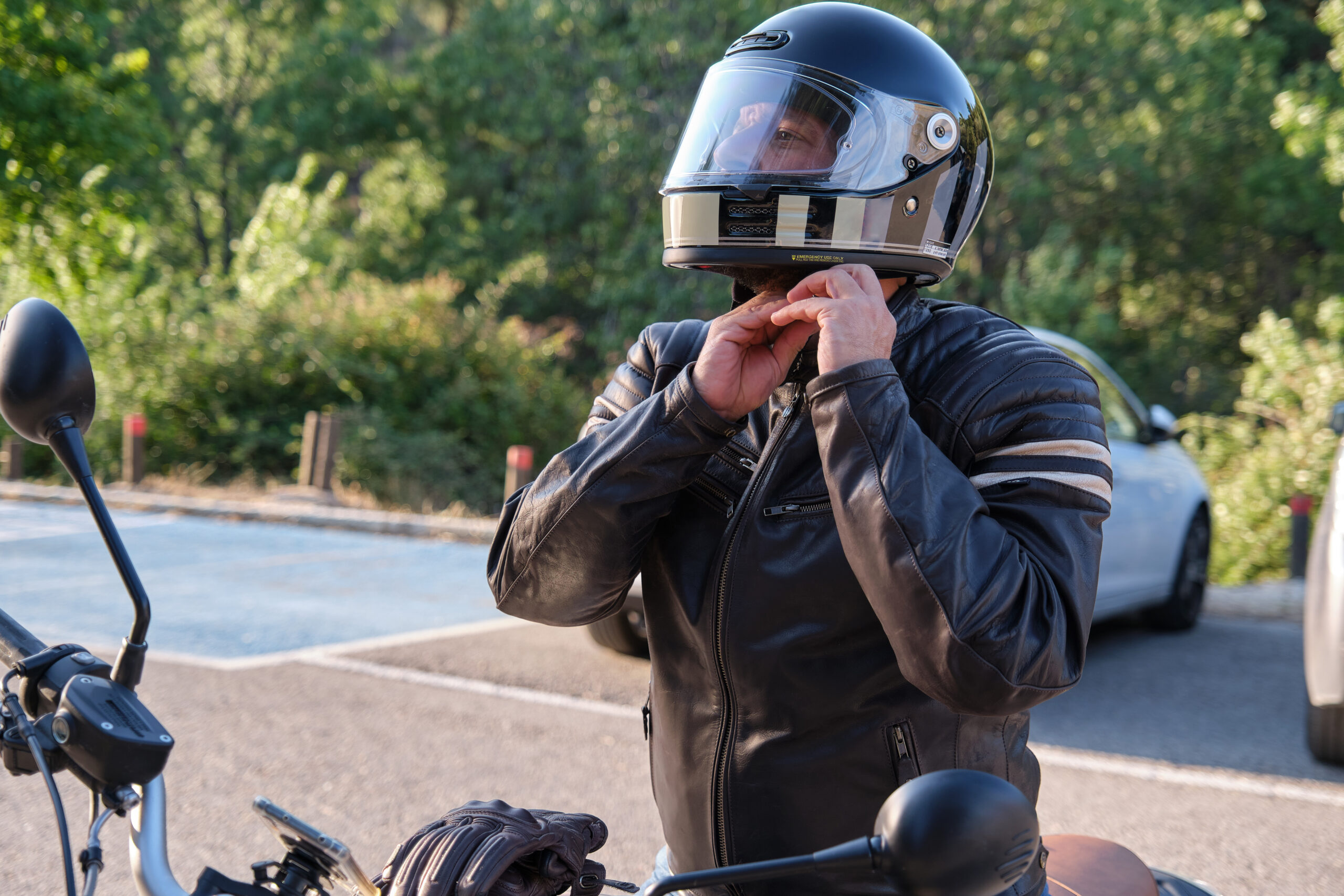 A biker puts on helmet before riding on motorbike | LeMaster Law Firm Motorcyclist wearing a black helmet and leather jacket fastening his helmet strap before riding.